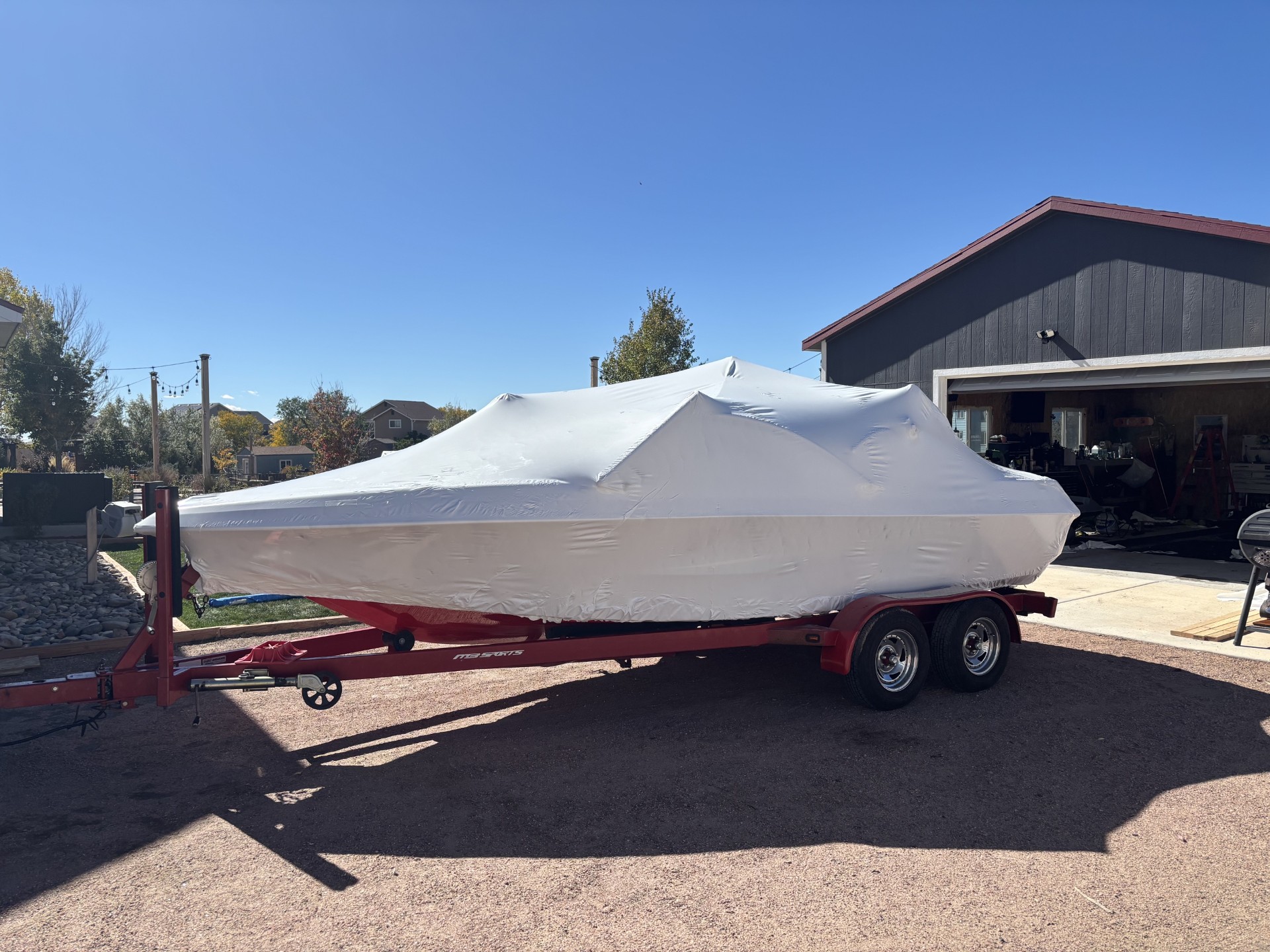 MB Sports boat covered in white shrink wrap on a red trailer outdoors
